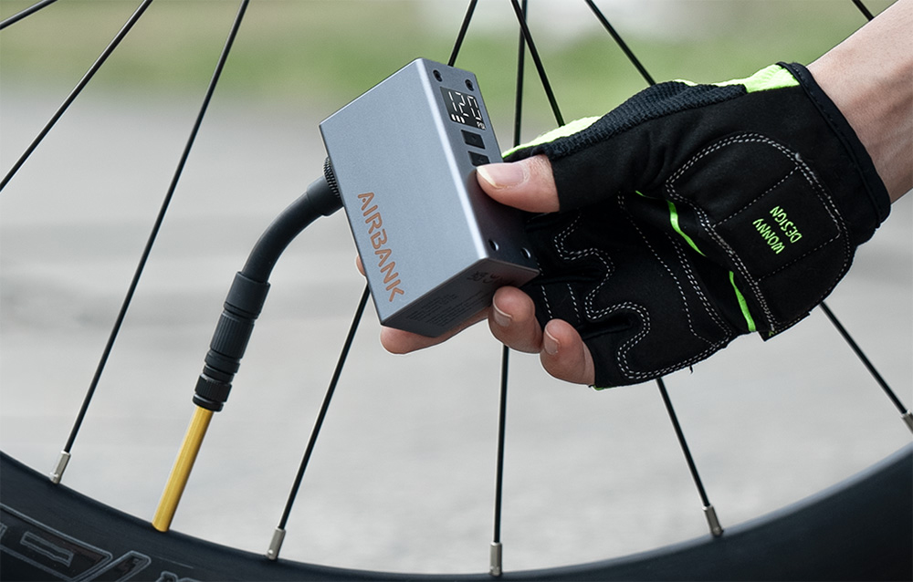 Szara pompka podłączona giętkim, czarnym wężykiem do zaworu sportowego koła rowerowego w trakcie pompowania.